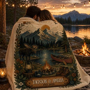 Può includere: Una coperta color crema con una scena all'aperto stampata raffigurante montagne, un lago, un alce, una canoa, un falò e una lanterna. Il design include un cartello in legno con il testo "JACKSON & AMELIA EST. 2026" e bordi floreali.