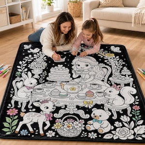 May include: A black rectangular blanket featuring a white line art illustration of a tea party scene with a princess, a rabbit, a squirrel, and a bear. The design includes a table with a teapot, cake, and teacups, surrounded by floral motifs.