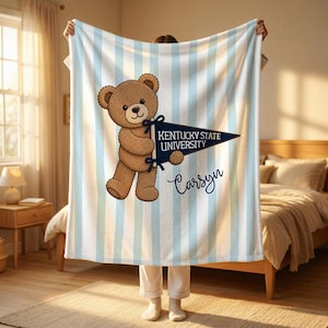 Könnte beinhalten: Eine blau-weiß gestreifte Decke mit einem braunen Teddybären, der eine Fahne hält. Auf der Fahne steht "Kentucky State University" und der Name "Carsyn". Die Decke ist aus weichem Material.