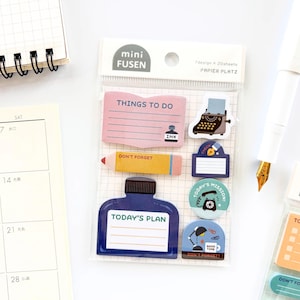 May include: A clear plastic package containing various sticky notes with different shapes and designs. The notes feature text like "Things to Do" and "Today's Plan," along with illustrations of a typewriter, pencil, and ink bottle. The color palette includes pink, blue, yellow, and brown.