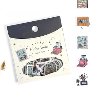 May include: A package of "Flake Seal" stickers featuring various designs, including a pink typewriter, postage stamps, and stationery items. The packaging is white with a black top and a small hole for hanging.
