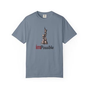 May include: A light blue t-shirt featuring a chess piece graphic. The graphic shows a pawn and a queen, with the word "imPossible" in red. The shirt is made of a soft material and has a crew neck.