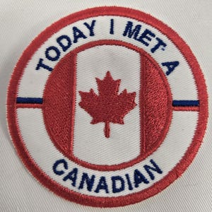 Może przedstawiać: Okrągła, haftowana naszywka z flagą Kanady i napisem "TODAY I MET A CANADIAN". Naszywka ma białe tło z czerwonymi i niebieskimi akcentami.