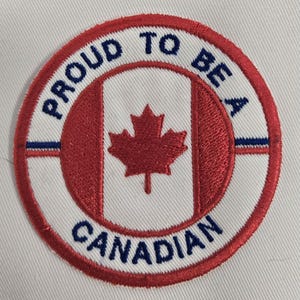May include: Embroidered patch with the text "PROUD TO BE A CANADIAN" in blue, surrounding a red maple leaf and the Canadian flag. The patch is circular with a white background and red and blue accents.