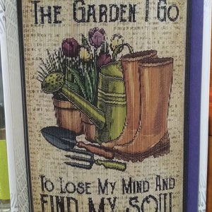 May include: A brown and tan woven wall hanging with the text "AND INTO THE GARDEN I GO TO LOSE MY MIND AND FIND MY SOUL". The image features a watering can, gardening gloves, a trowel, and a bouquet of flowers.