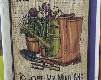May include: A brown and tan woven wall hanging with the text "AND INTO THE GARDEN I GO TO LOSE MY MIND AND FIND MY SOUL". The image features a watering can, gardening gloves, a trowel, and a bouquet of flowers.