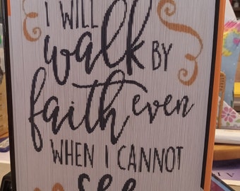 May include: A white book with a folded paper cover. The cover has a black and gold design with the text "I will walk by faith even when I cannot see" and "2 Corinthians 5:7".