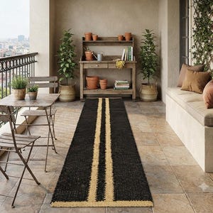May include: A long rectangular runner rug featuring a dark black woven texture with two parallel light beige stripes running down the center and a matching beige border at the bottom edge, positioned on a tiled balcony floor.