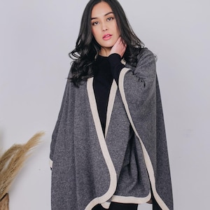 May include: A gray cape with cream-colored trim. The cape is draped over the shoulders and has a flowing design. The word "TRIKAYA" is visible in the lower left corner.