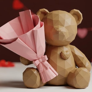 May include: A geometric brown teddy bear holding a pink paper bouquet tied with a bow. Two lit candles and red heart decorations are in the background. A red gift box is also visible.