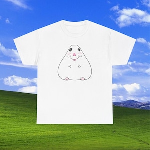 Pode incluir: Uma t-shirt branca de manga curta com um gráfico central de uma criatura redonda e branca de estilo cartoon, com nariz cor-de-rosa, pequenas bochechas rosadas e uma boca sorridente simples. A criatura tem olhos pretos e patas minúsculas.
