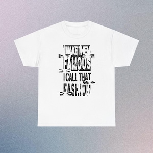 Può includere: Una t-shirt bianca a maniche corte con una stampa grafica nera sul petto. Il design include il testo 'I MAKE THEM FAMOUS I CALL THAT EASYLIFE' in un carattere tipografico usurato e a blocchi, intervallato da diversi paia di occhi umani.