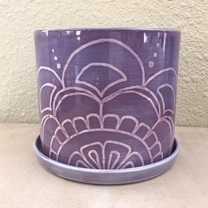 May include: A purple ceramic planter with a white geometric design. The planter has a matching saucer.