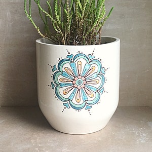 May include: A white ceramic planter with a blue, green, and orange floral design. The planter is filled with a green succulent plant.