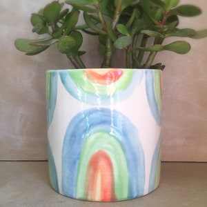 May include: A white ceramic planter with a rainbow design. The planter is filled with a green succulent plant.