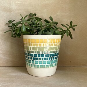 May include: A ceramic planter with a yellow, green, and blue mosaic design. The planter is filled with a green succulent plant.