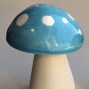 May include: A ceramic mushroom figurine with a blue glaze and white polka dots. The mushroom has a white stem.