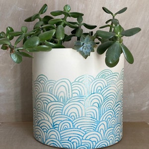 May include: White ceramic planter with a blue and white wave pattern. The planter is filled with a green succulent plant.