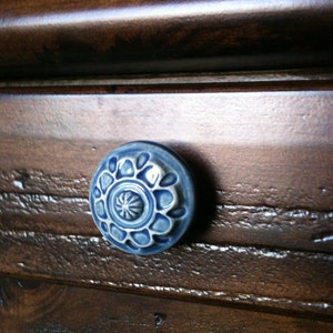 Può includere: Una maniglia per cassetto in ceramica blu e bianca con un motivo floreale. La maniglia è montata su un cassetto in legno marrone scuro.