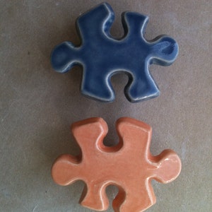 May include: Two ceramic puzzle pieces, one blue and one orange, on a brown background.