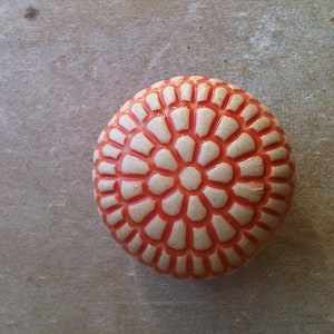 Puede incluir: Un pomo redondo de cerámica con fondo blanco y diseño floral naranja.