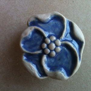 Può includere: Un fiore in ceramica blu con un centro rialzato, che ricorda un fiore con un gruppo di boccioli. Il fiore è smaltato con una finitura lucida.