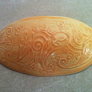 May include: A light orange ceramic dish with an intricate floral design. The dish is oval shaped and has a glossy finish.