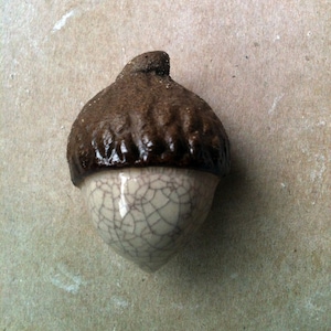 May include: A ceramic acorn ornament with a brown top and a white bottom with a crackled glaze.