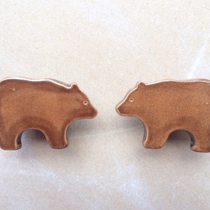 May include: Two brown ceramic bear figurines facing each other. The bears are simple in design and have a smooth, glossy finish.
