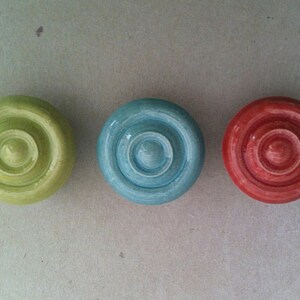 May include: Three wooden game pieces with concentric circles. The pieces are green, blue, and red.