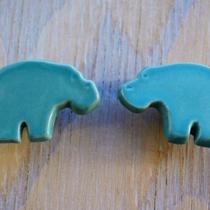 May include: Two teal blue ceramic hippopotamus figurines facing each other.