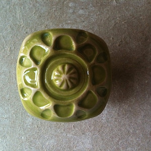 Peut inclure: Un bouton en céramique vert avec un motif circulaire en relief. Le bouton a une finition brillante et une surface légèrement texturée.