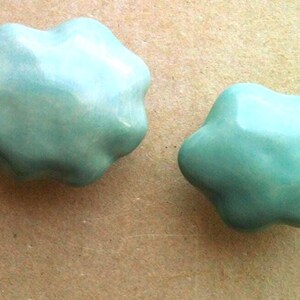 May include: Two light blue ceramic ornaments shaped like clouds. The ornaments have a smooth, glossy finish.