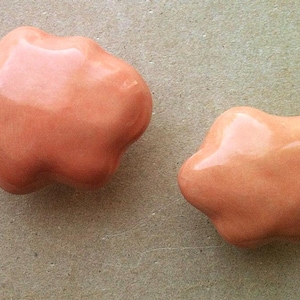 May include: Two peach-coloured ceramic ornaments shaped like irregular clouds. The ornaments are smooth and glossy.