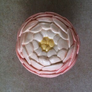 May include: A ceramic flower with a pink and white exterior and a yellow centre. The flower has a textured surface that resembles petals.