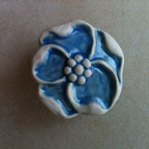 May include: A ceramic flower-shaped knob with a blue glaze and a white center. The knob has a raised design of five petals and a cluster of five white dots in the center.