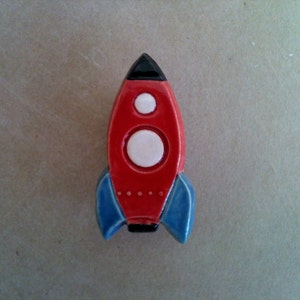 May include: A red and blue ceramic rocket ship with white circles on the body. The rocket ship is a decorative object.