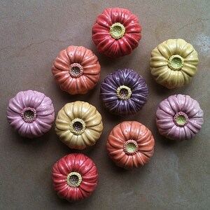 May include: Ten ceramic flower-shaped knobs in various shades of pink, orange, yellow, and purple. Each knob has a raised centre with a yellow circle in the middle.