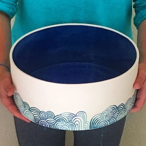 May include: A white ceramic bowl with a blue interior and a blue and green wave design around the rim.