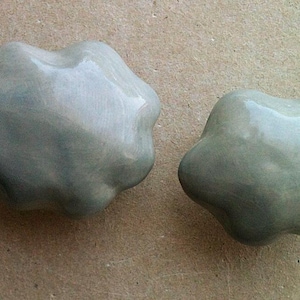 May include: Two smooth, grey ceramic cloud-shaped ornaments. The clouds have a slightly textured surface and a glossy finish.