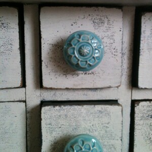 May include: A white wooden cabinet with multiple drawers, each with a blue ceramic knob featuring a floral design.