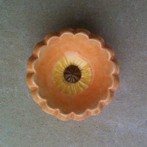 May include: A small, ceramic dish with a scalloped edge. The dish is peach-coloured with a yellow and brown flower design in the centre.