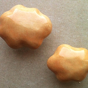 May include: Two ceramic knobs in a light orange colour. The knobs have a unique, irregular shape with rounded edges.