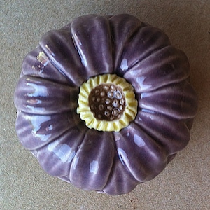 May include: A ceramic flower with a purple body and a yellow centre. The flower has a glossy finish and is shaped like a daisy.