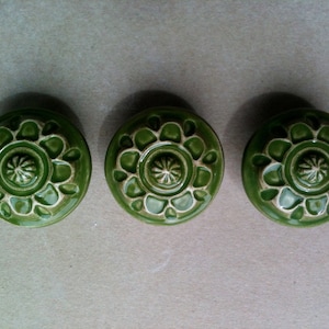 May include: Three green ceramic knobs with a white floral design. The knobs have a raised centre with a smaller floral design.