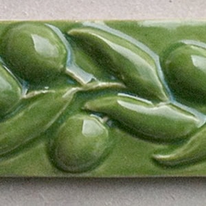May include: A green ceramic tile with a raised design of olive branches and olives. The tile is glazed and has a smooth surface.