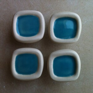May include: Four white ceramic knobs with a square shape and a recessed blue square in the centre.