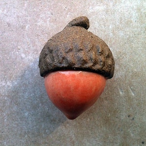 Peut inclure: Une décoration d'automne en forme de gland en céramique avec un chapeau brun et un fond orange vif.