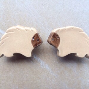 May include: Two ceramic sheep figurines with brown faces and white bodies. The sheep are facing each other.