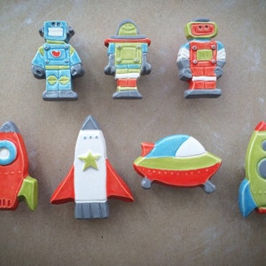 May include: A set of eight ceramic space-themed ornaments, including robots, rockets, and a flying saucer. The ornaments are painted in bright colors, including red, green, blue, and yellow.